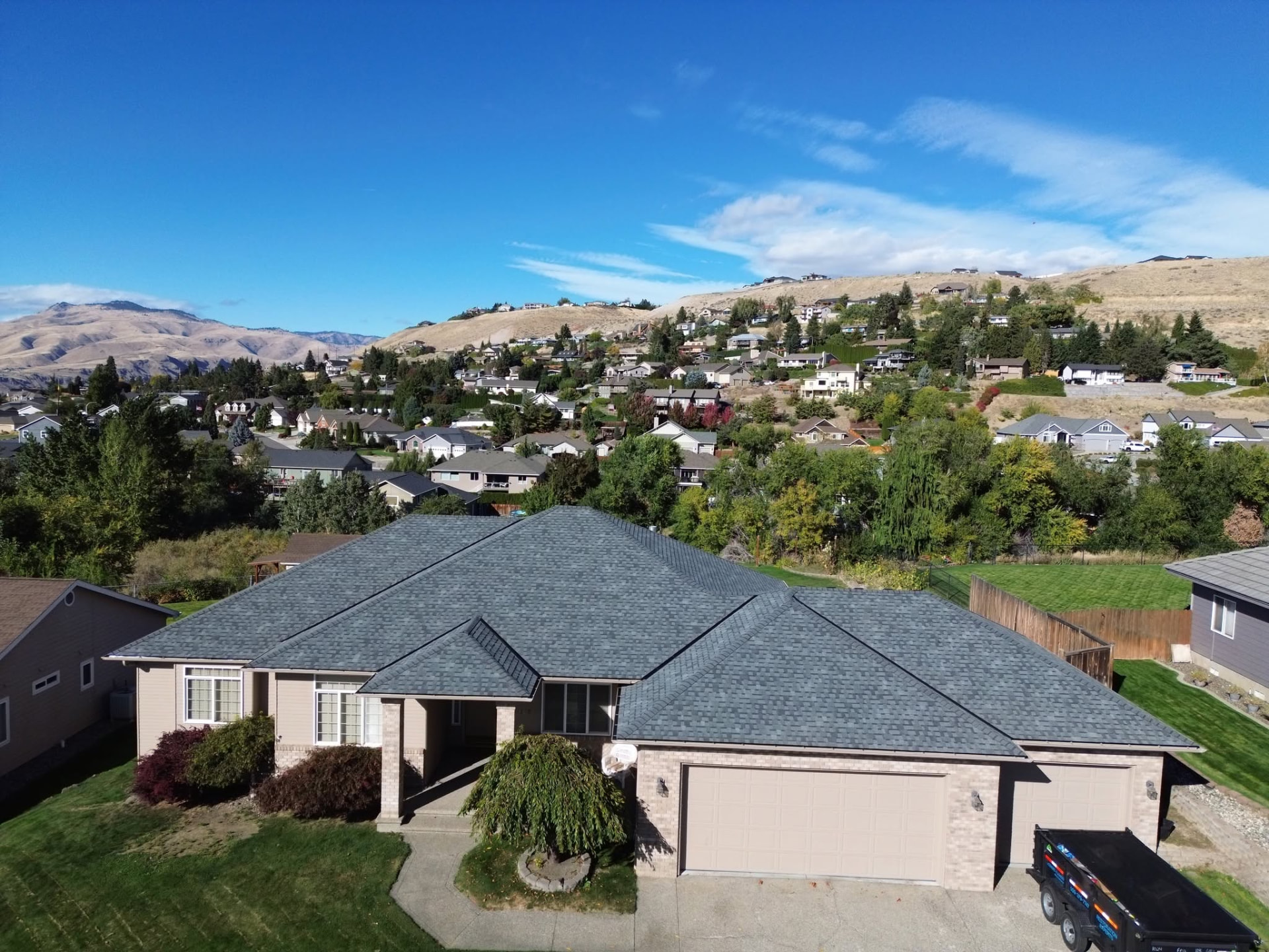 Finished charcoal shingle roof with sunlit hills behind the home